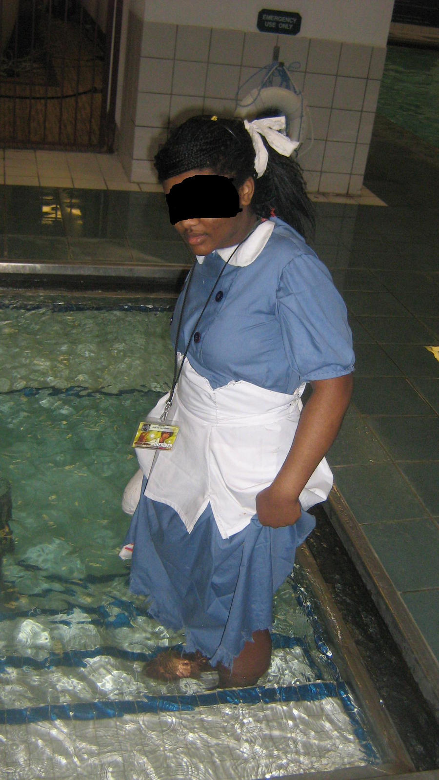 a picture of a cosplay of a Little Sister from Bioshock 1. the dress is light blue. The cosplayer is standing in the water of a swimming pool